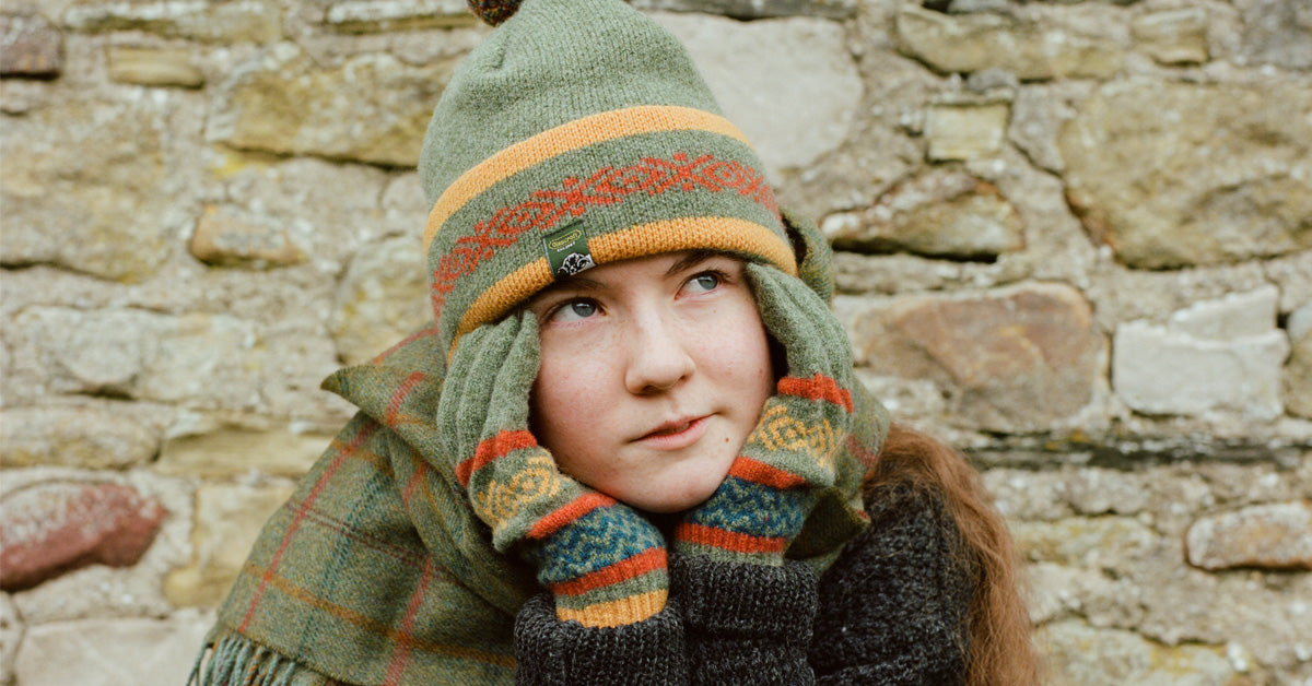 Woman with green knitted beanie hat, gloves and scarves in front of a wall