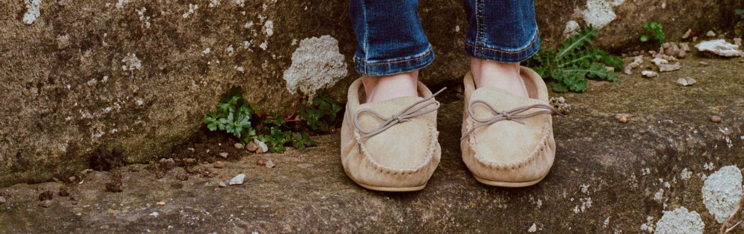 Close up of someone's feet wearing a pair of beige moccasins slippers on an outdoor stone step