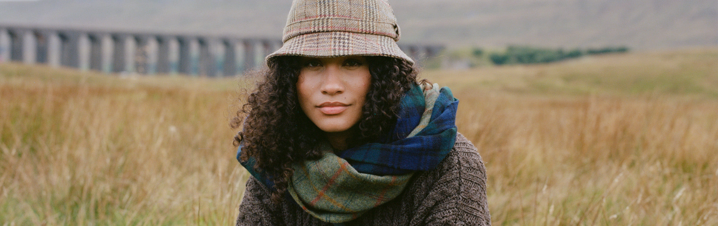 Women in front of viaduct wearing tweed hat, scarves and wool jumper