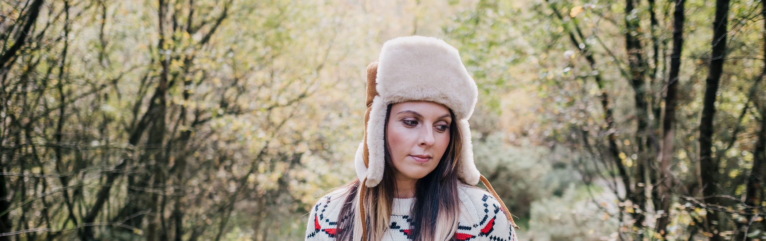 Woman wearing sheepskin trapper hat and white nordic pattern jumper in a forest