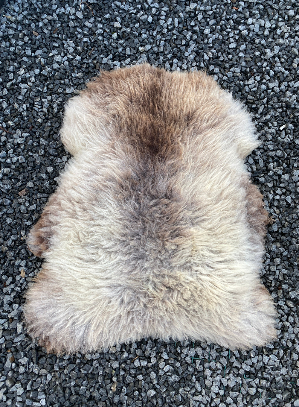 Brown and beige sheepskin rug on gravel