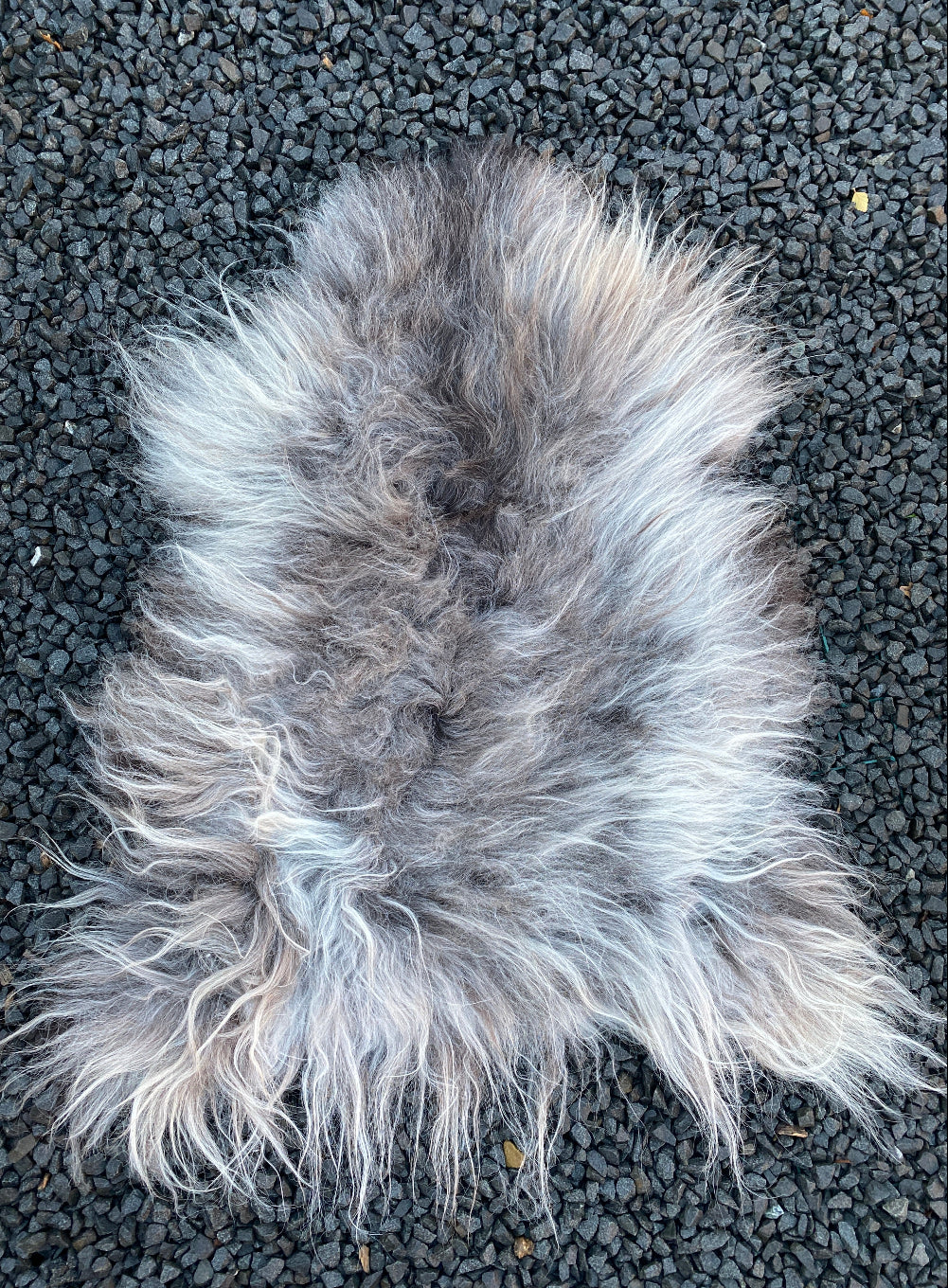 Grey sheepskin rug laid flat on gravel
