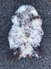 Brown and cream sheepskin rug laid flat on gravel