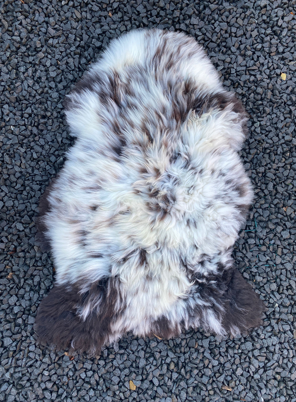 Brown and cream sheepskin rug laid flat on gravel