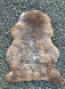 Brown and grey sheepskin rug laid flat on gravel