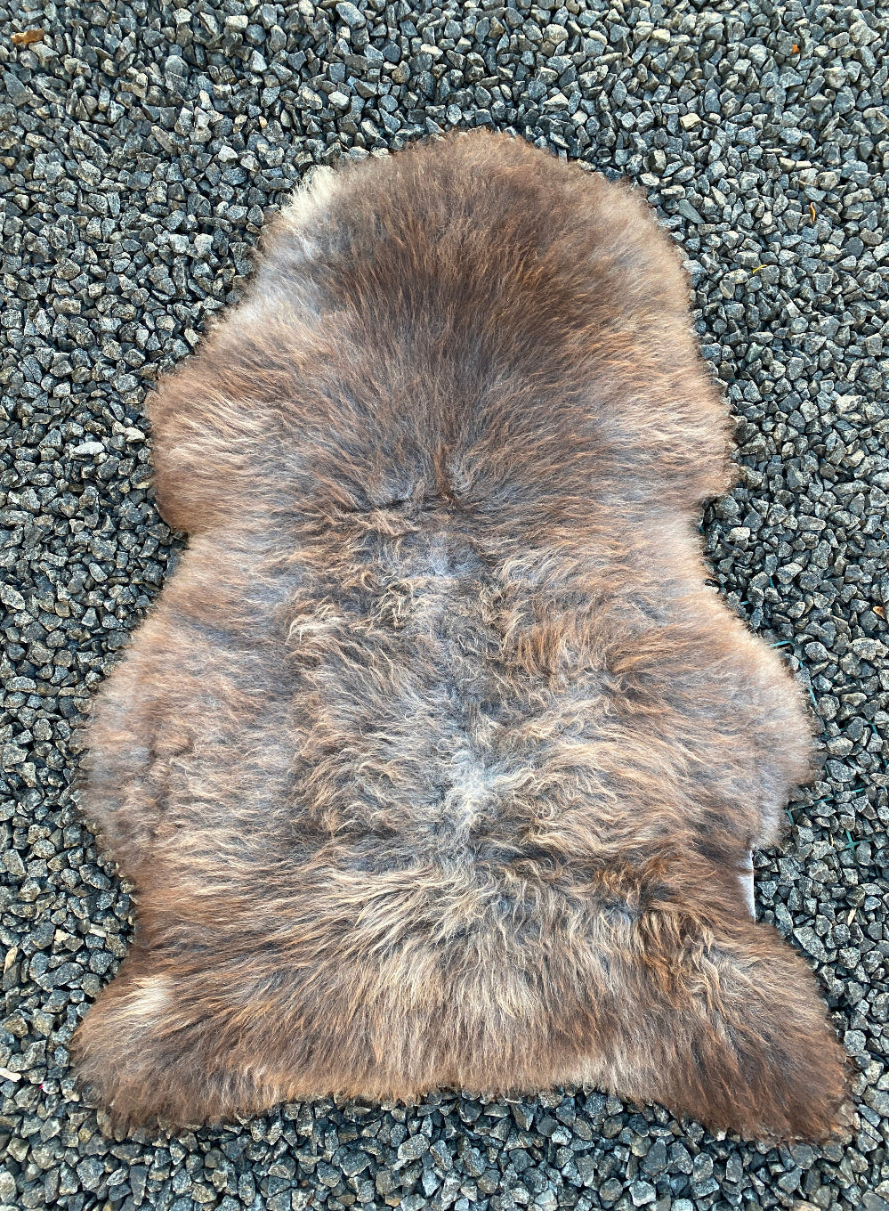 Brown and grey sheepskin rug laid flat on gravel