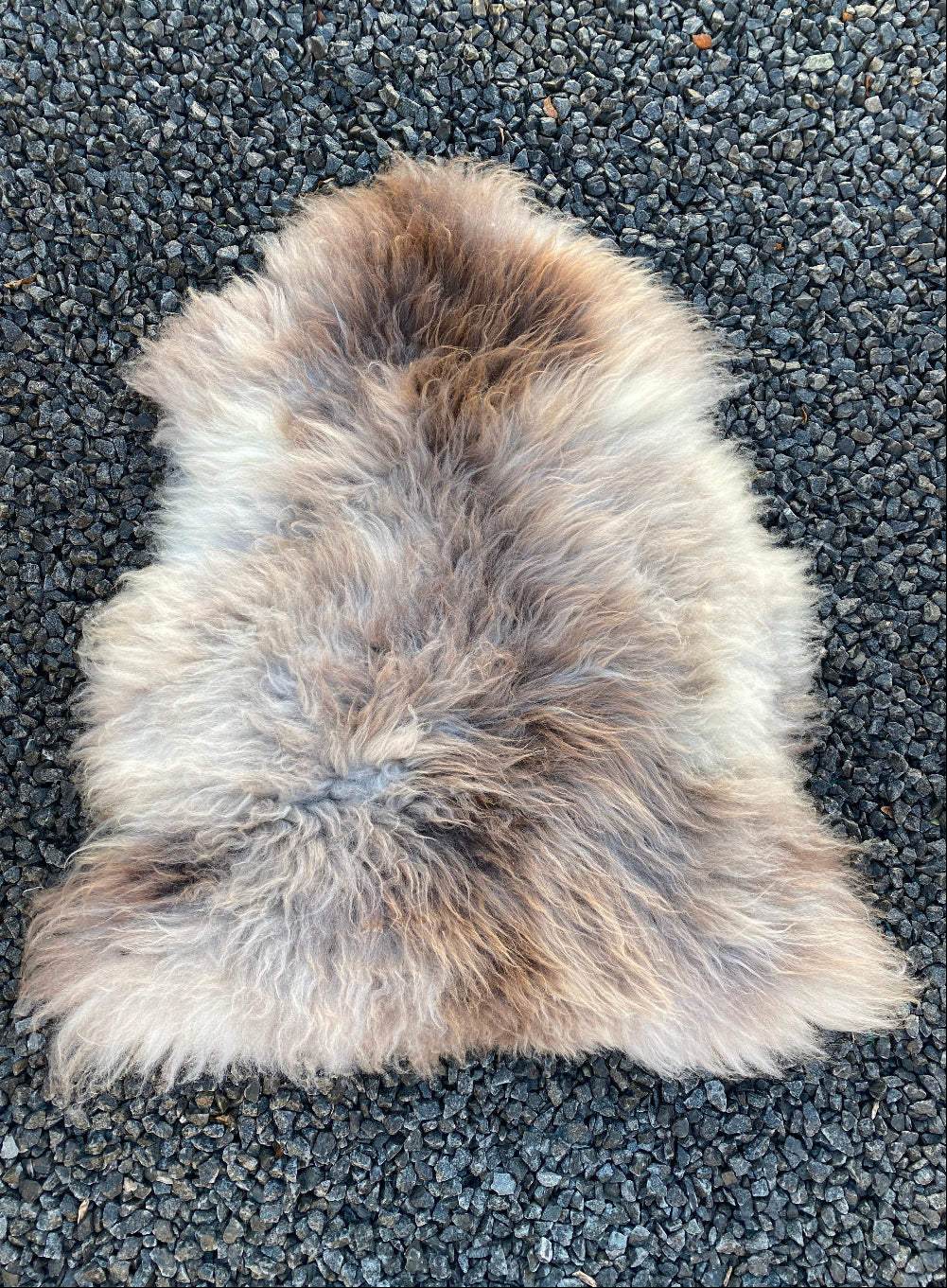 brown, cream and grey sheepskin rug laid flat on gravel