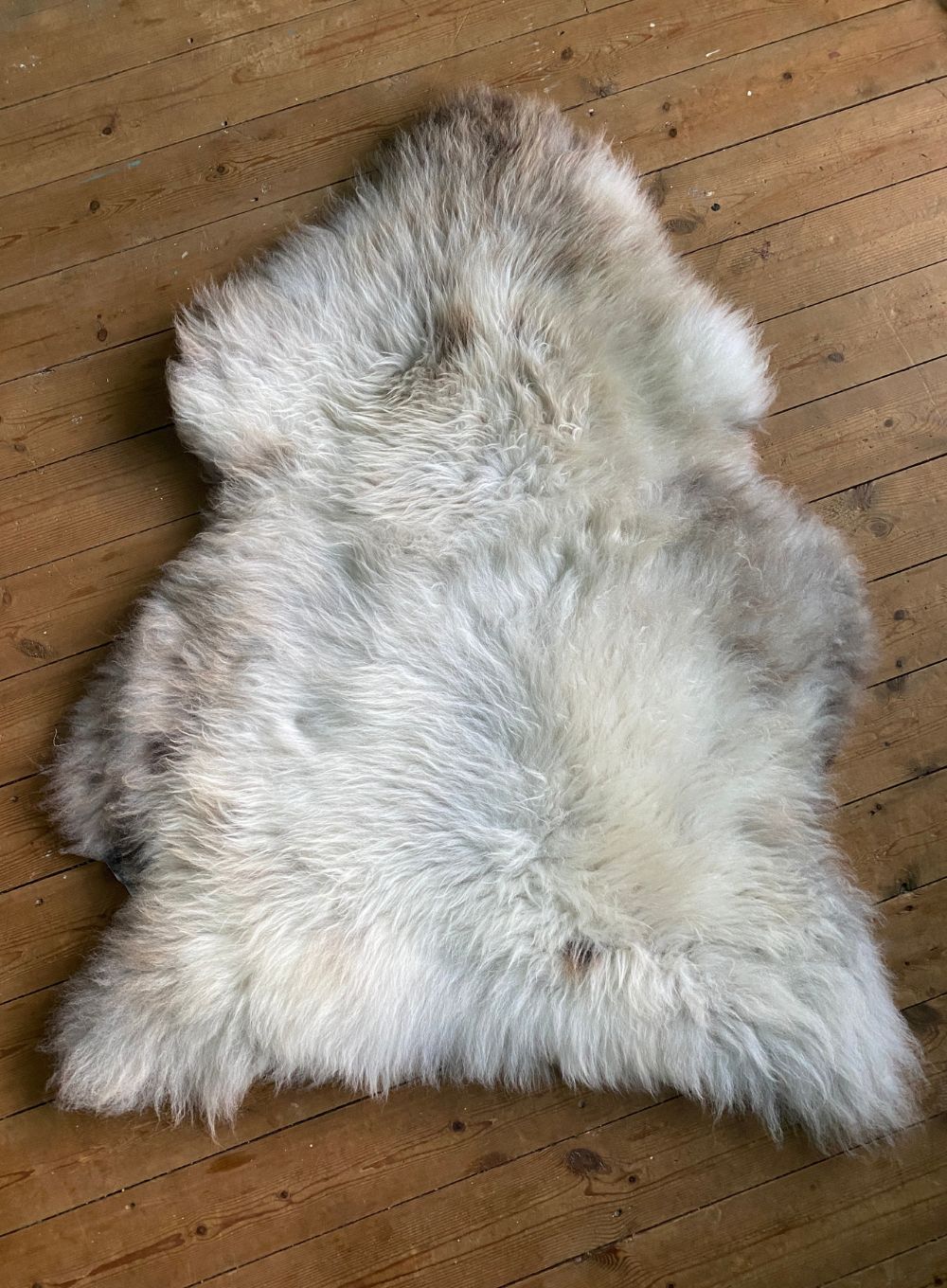Cream speckled sheepskin rug on wooden floor 