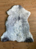 Grey sheepskin rug laid flat on wooden floor 