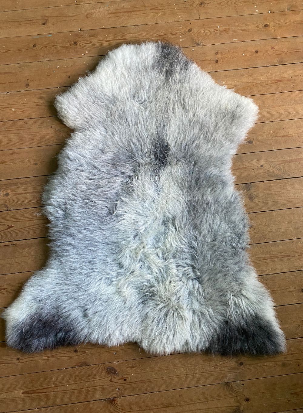 Grey sheepskin rug laid flat on wooden floor 
