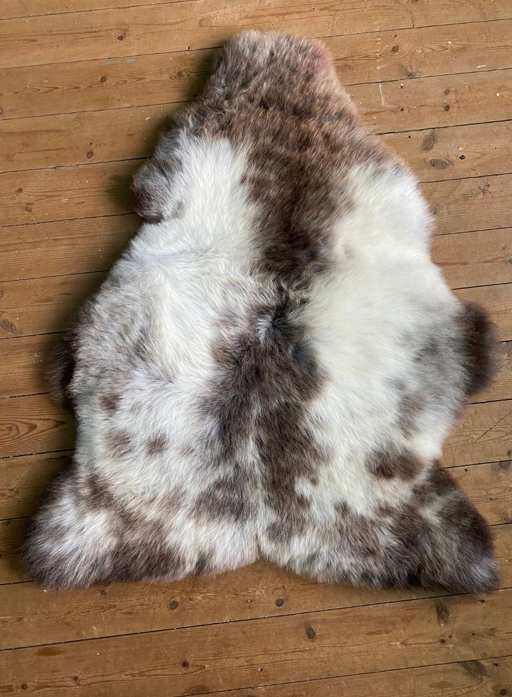 Brown and cream speckled sheepskin rug flat on wooden floor