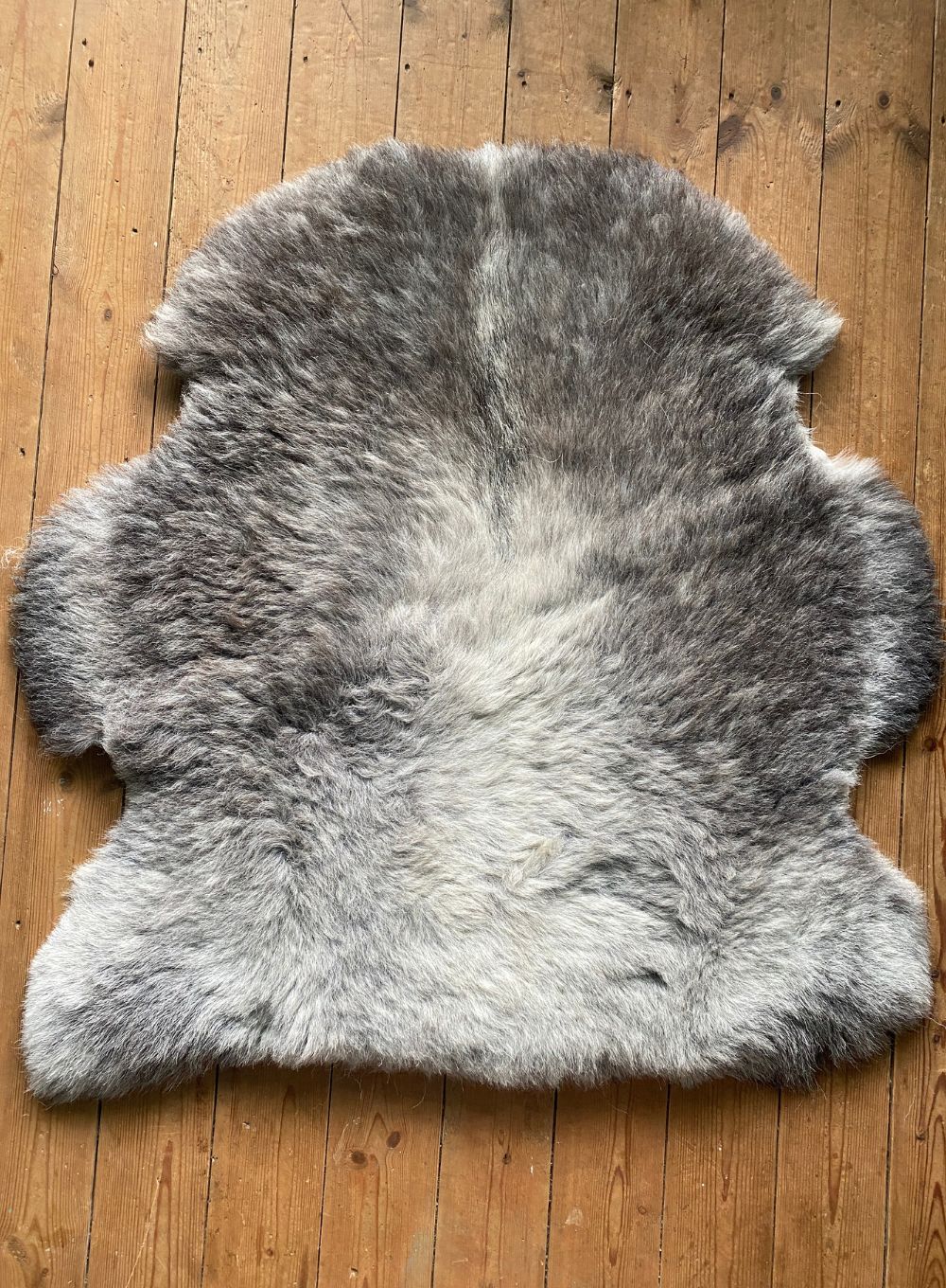 Grey sheepskin rug laid flat on wooden floor 
