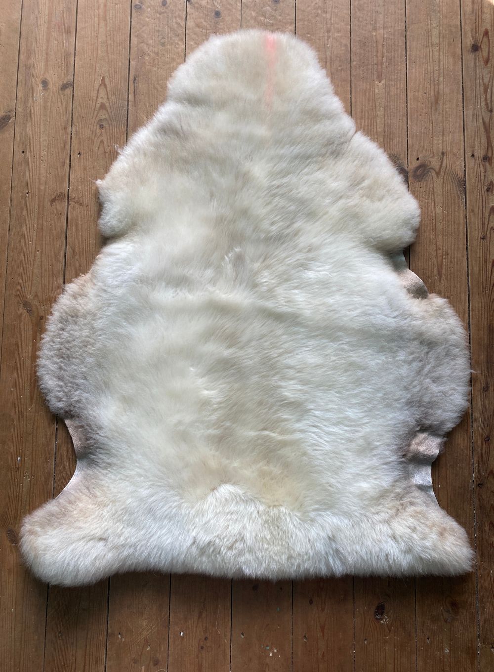 Cream sheepskin rug laid flat on wooden floor