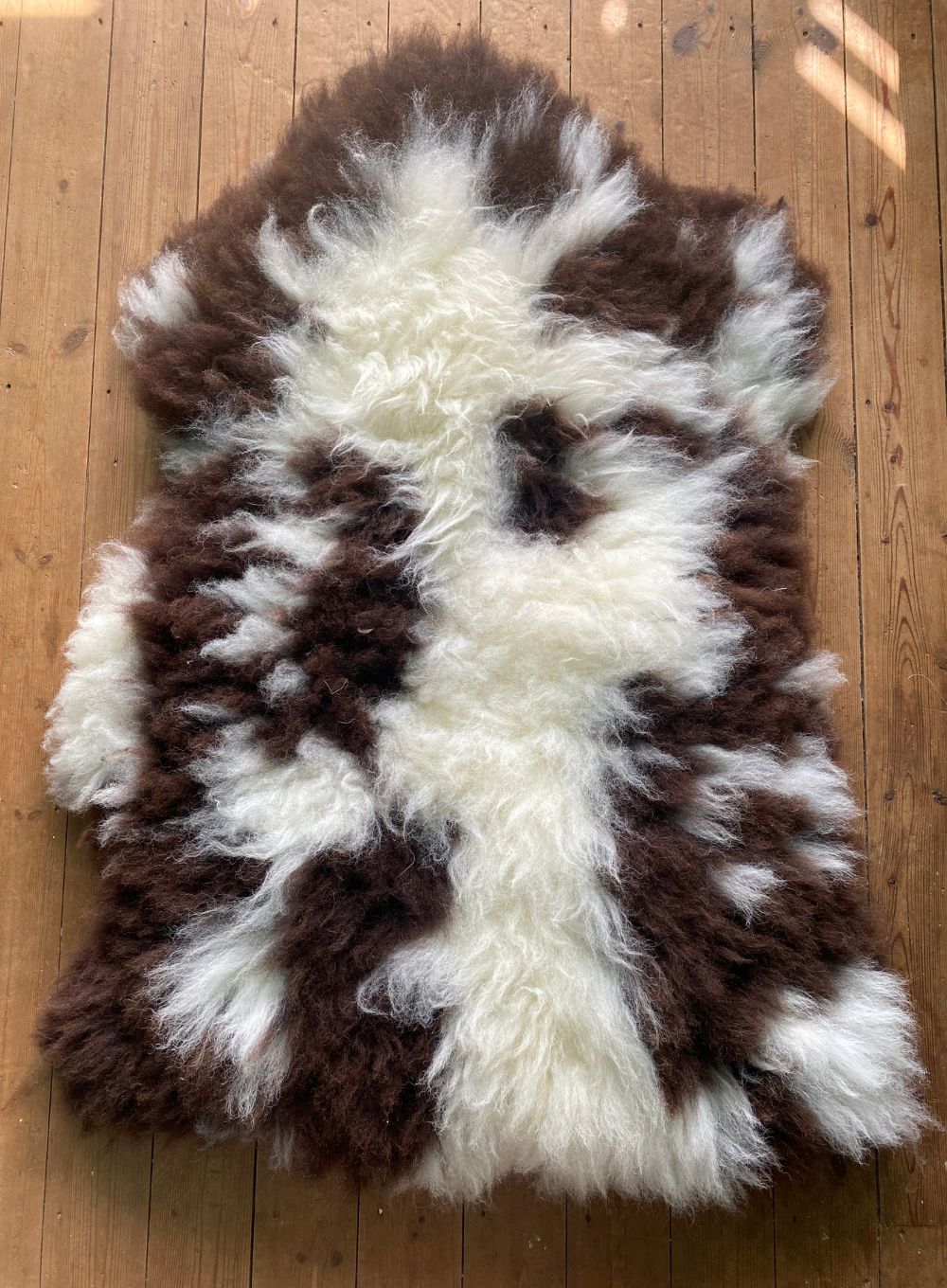 Cream and brown spotty sheepskin rug  laid flat on wooden floor