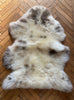 Cream speckled sheepskin rug laid flat on wooden floor
