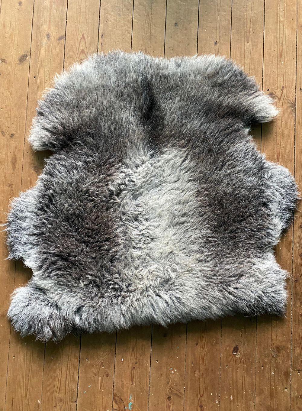 Grey sheepskin rug laid flat on wooden floor 