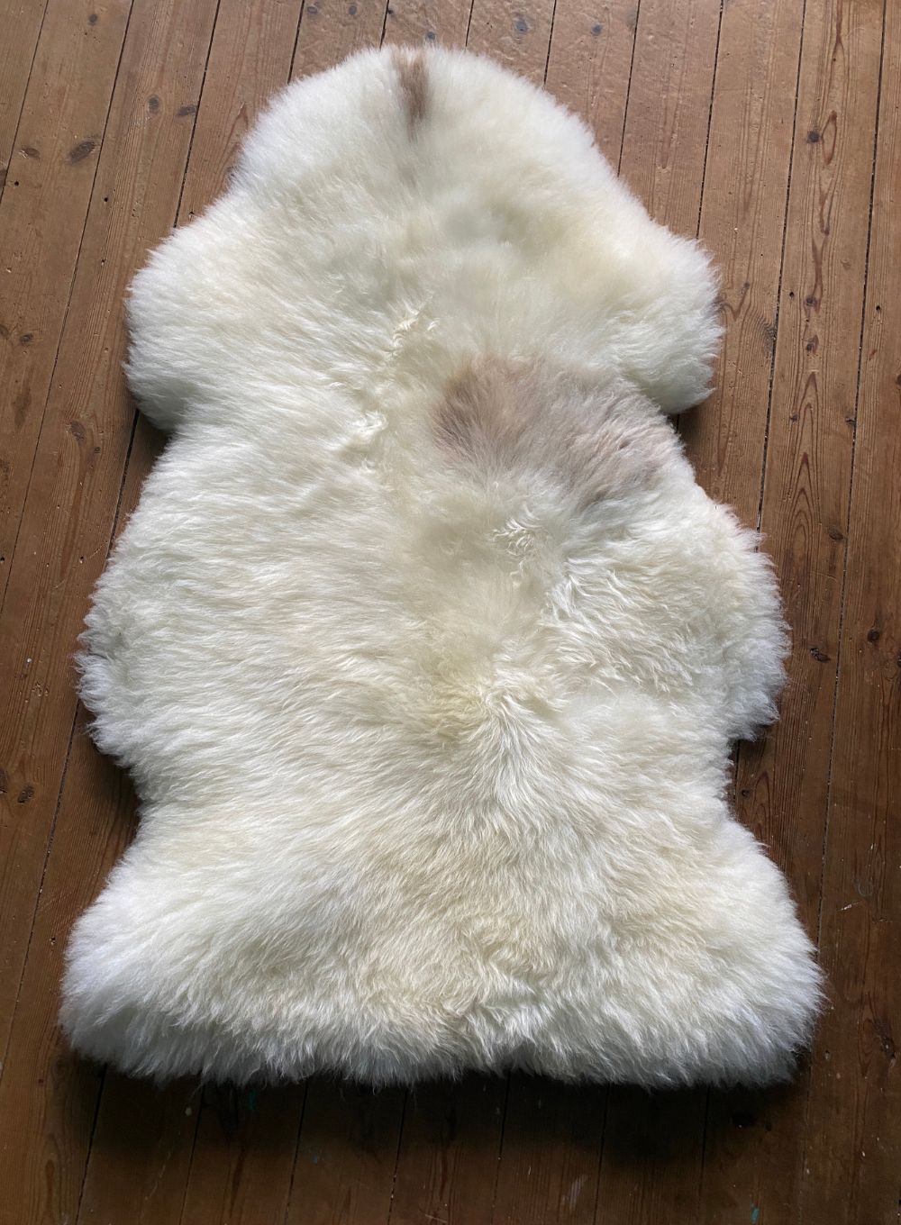 Cream sheepskin rug laid flat on wooden floor 