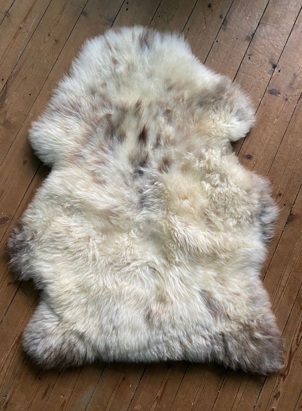 Cream speckled sheepskin rug laid flat on wooden floor 