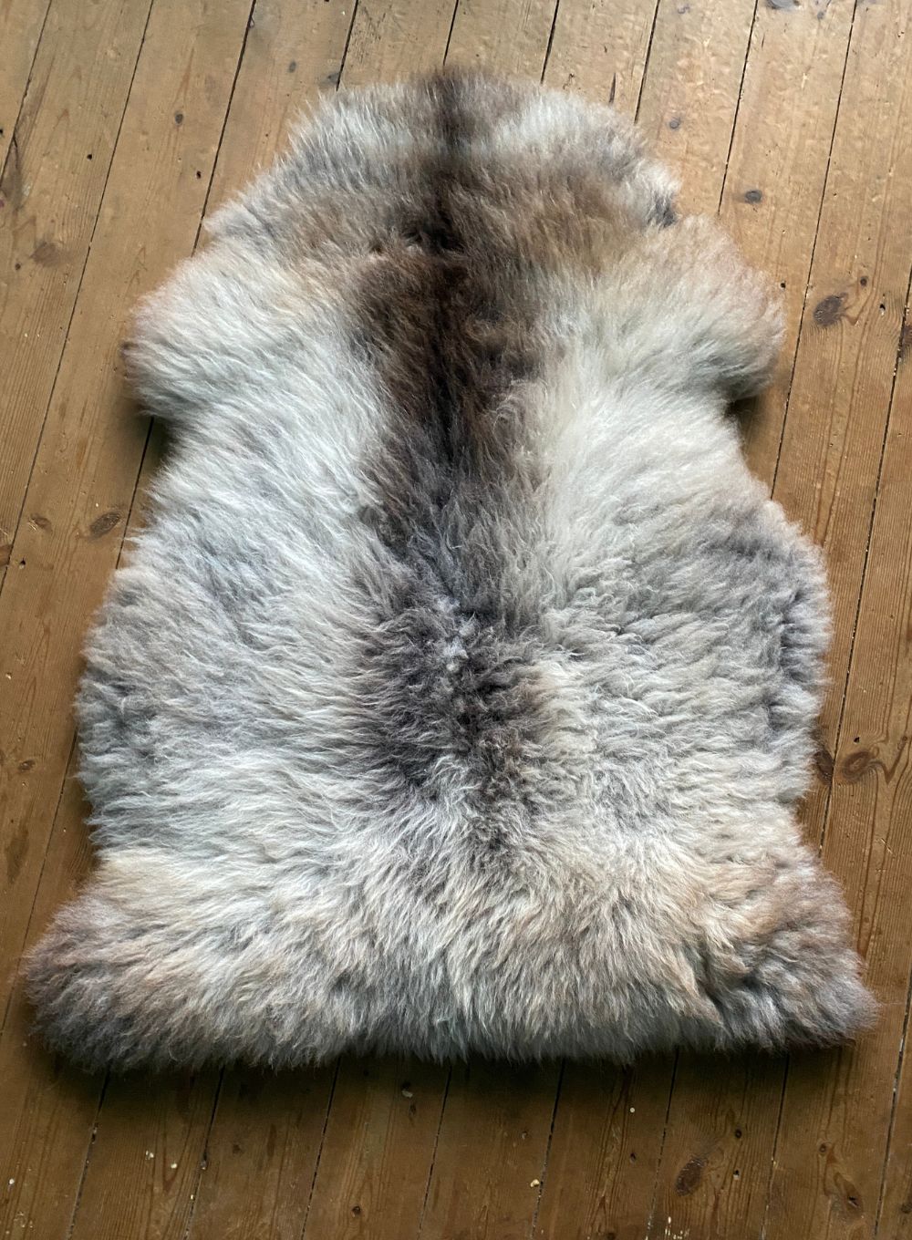Brown and grey sheepskin rug laid flat on wooden floor 