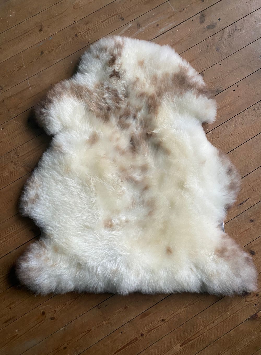 Cream speckled sheepskin rug on wooden floor