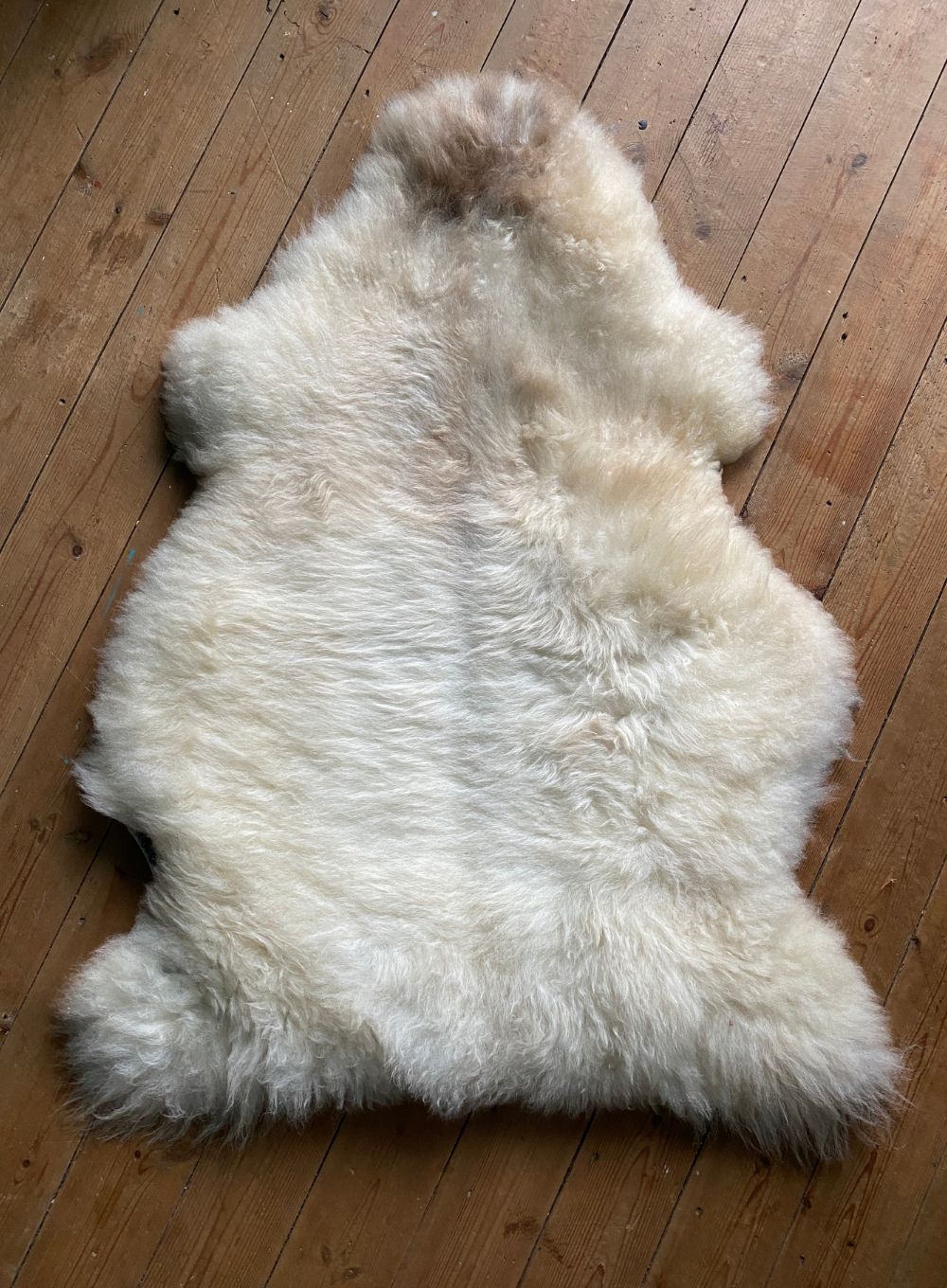 Cream speckled sheepskin rug on wooden floor