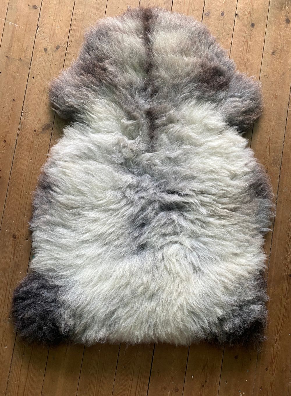 Grey and cream sheepskin rug on wooden floor 