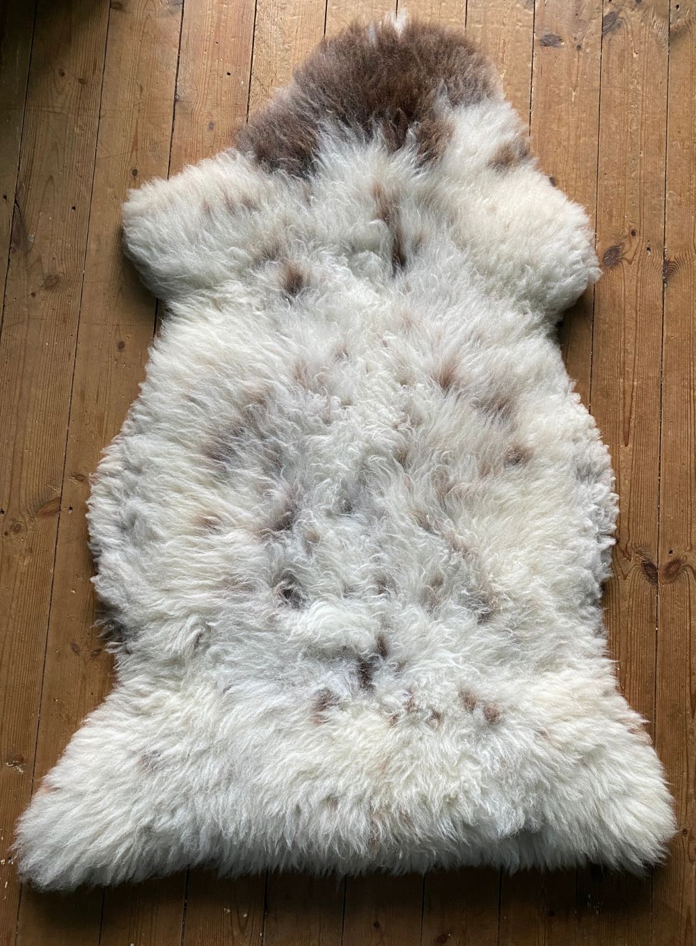 Cream and brown speckled sheepskin rug laid flat on wooden floor