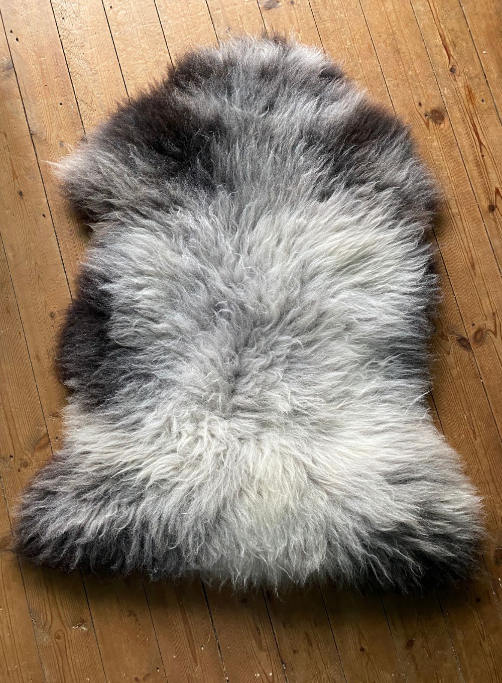 Grey sheepskin rug on wooden floor 