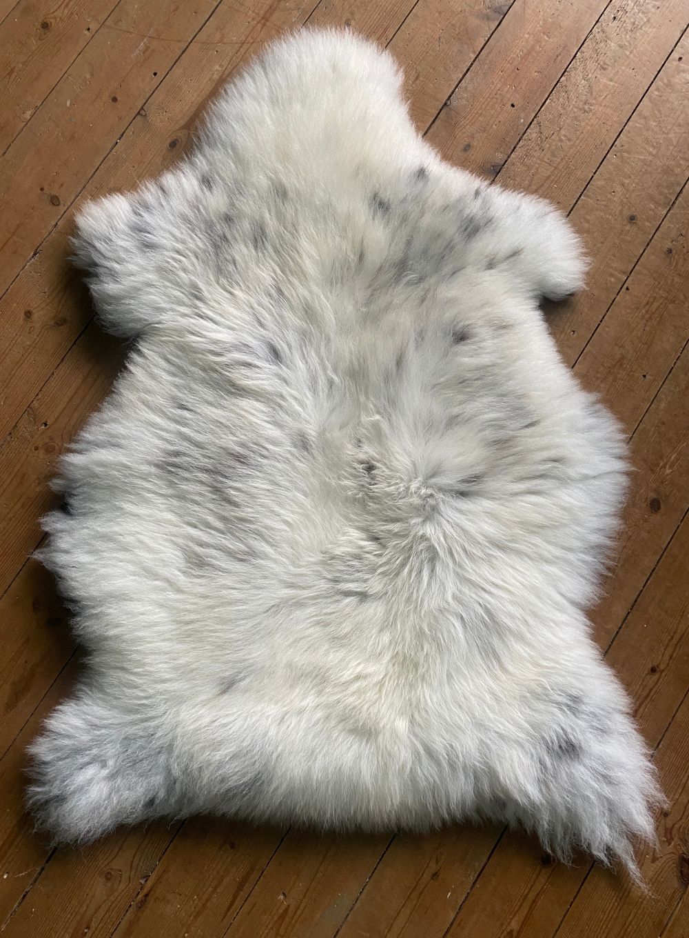 Cream speckled sheepskin rug on wooden floor