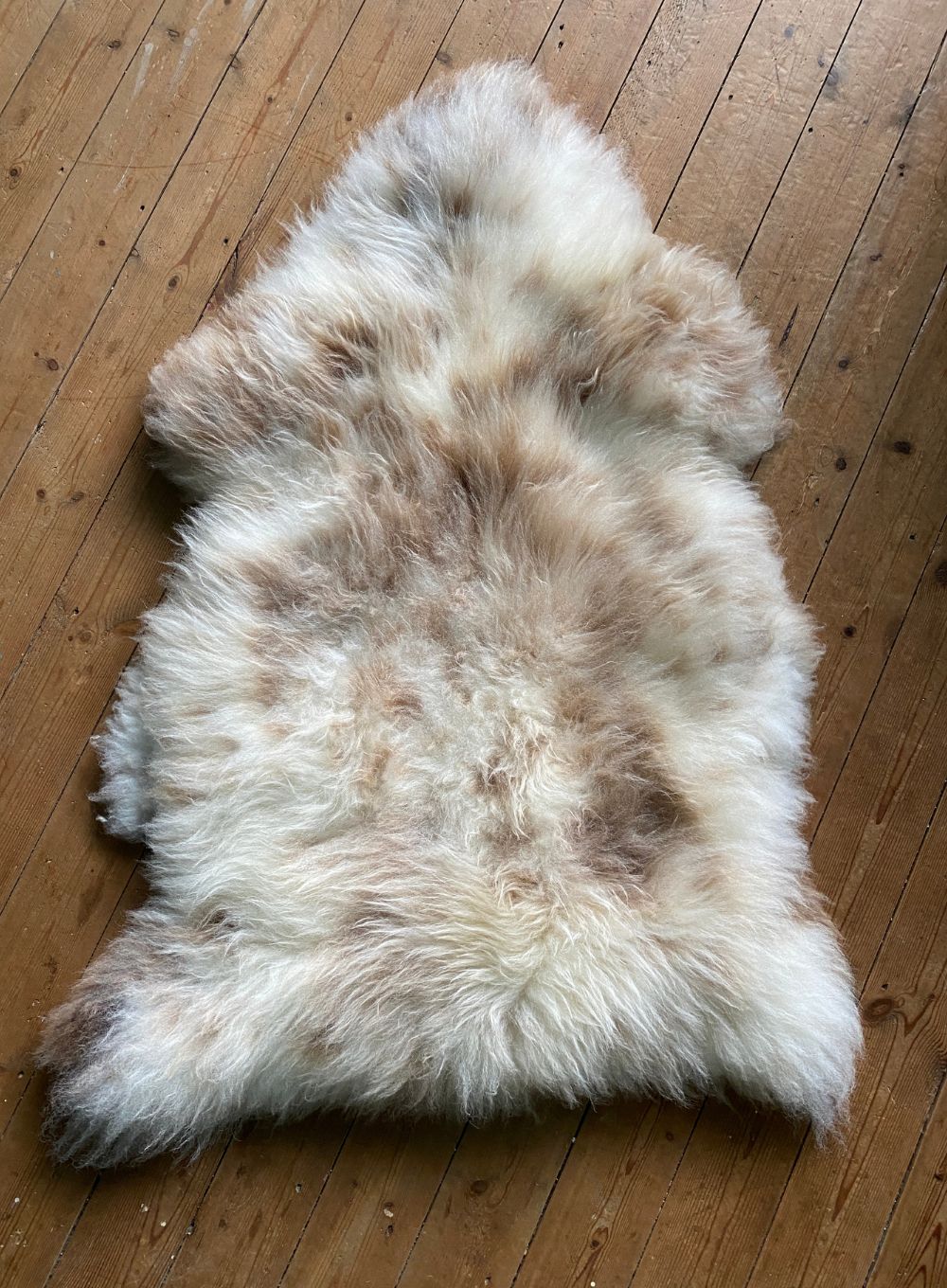 Cream speckled sheepskin rug on wooden floor 
