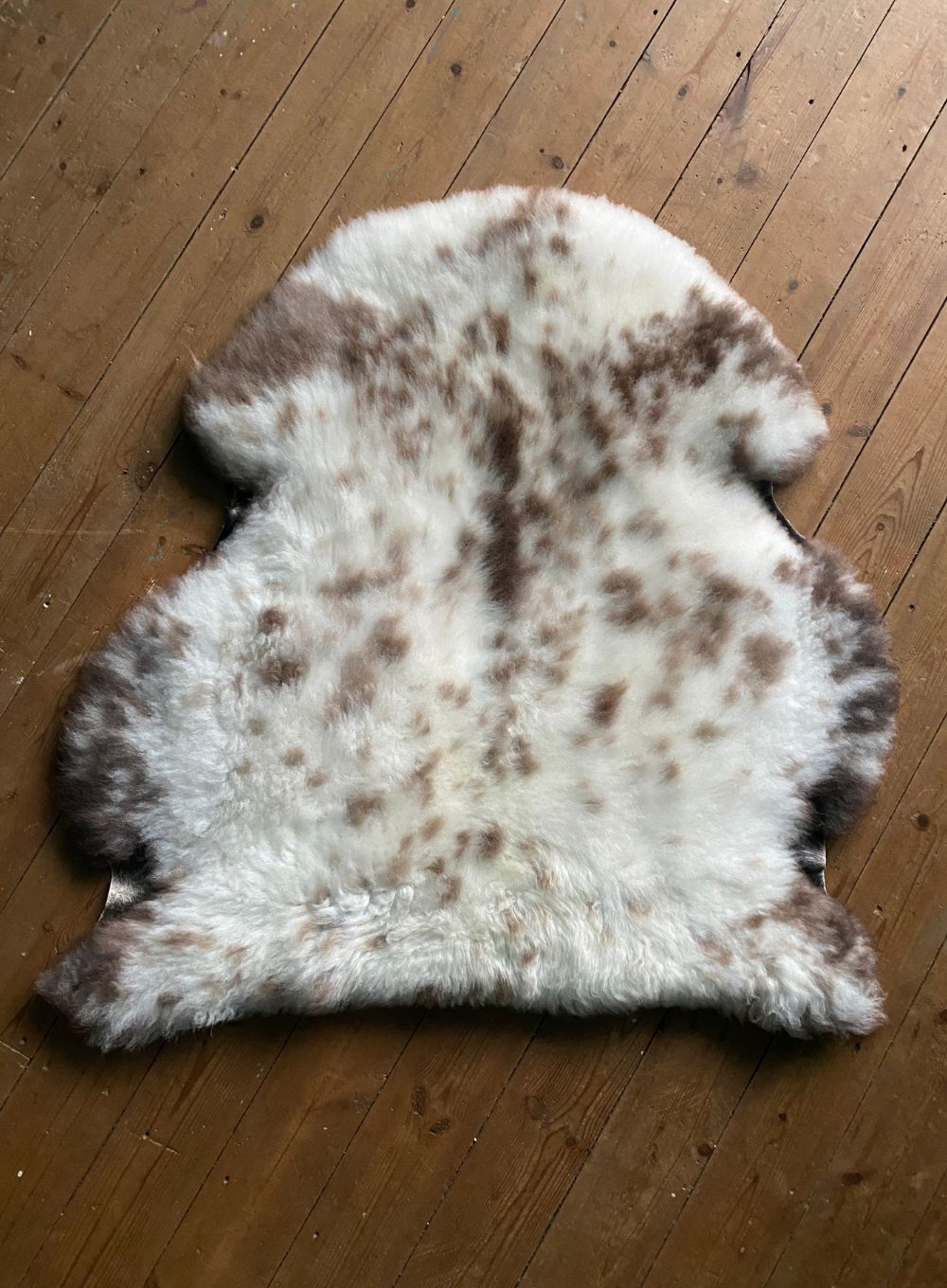 Cream speckled sheepskin rug on wooden floor 