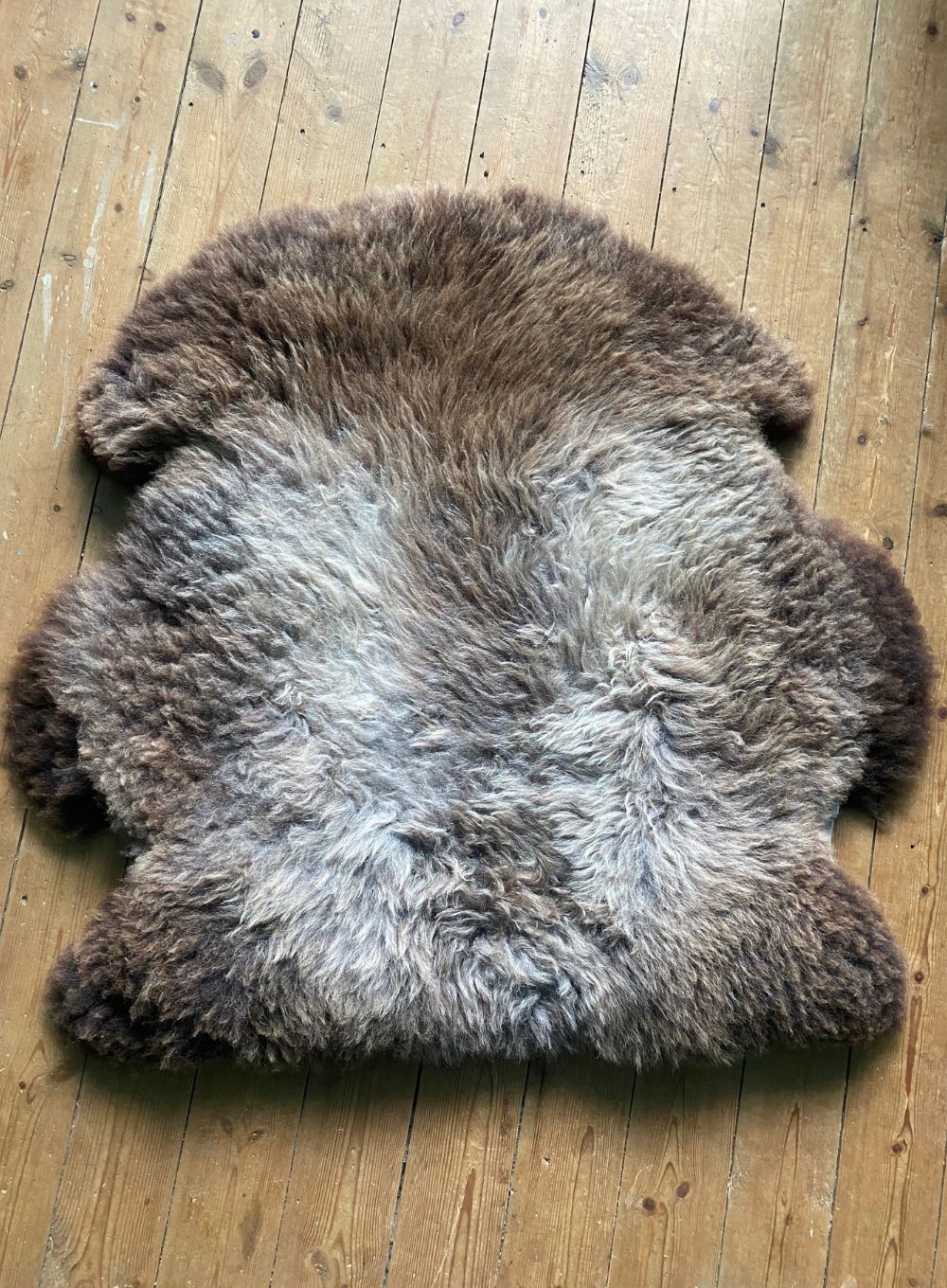 Grey and brown sheepskin rug on wooden floor 