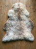 Cream speckled sheepskin rug laid flat on wooden floor