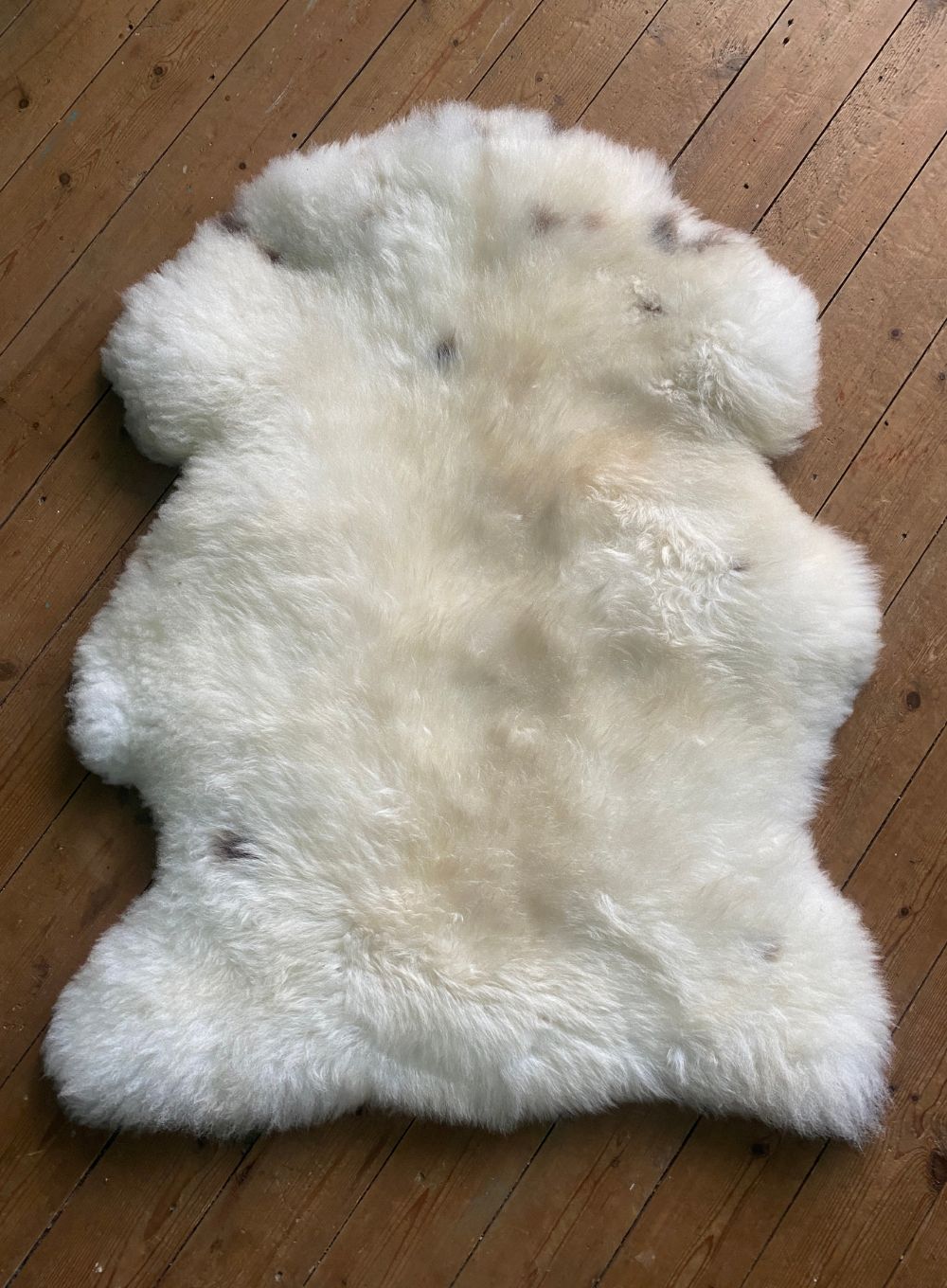 Cream speckled sheepskin rug on wooden floor 