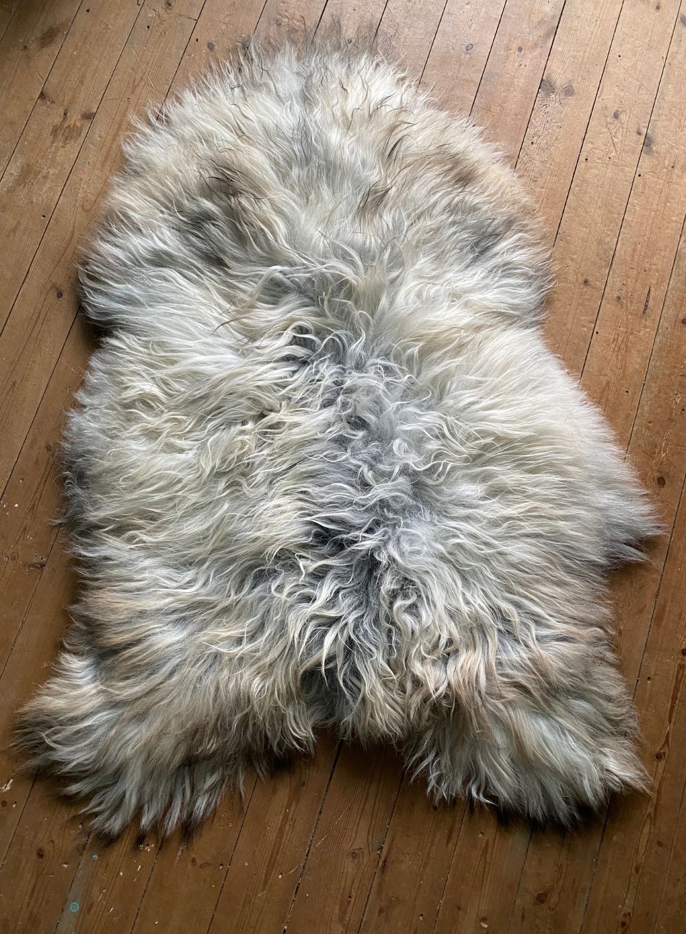Grey and cream long haired sheepskin rug on wooden floor
