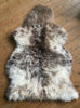 Cream and brown speckled sheepskin rug laid flat on wooden floor 