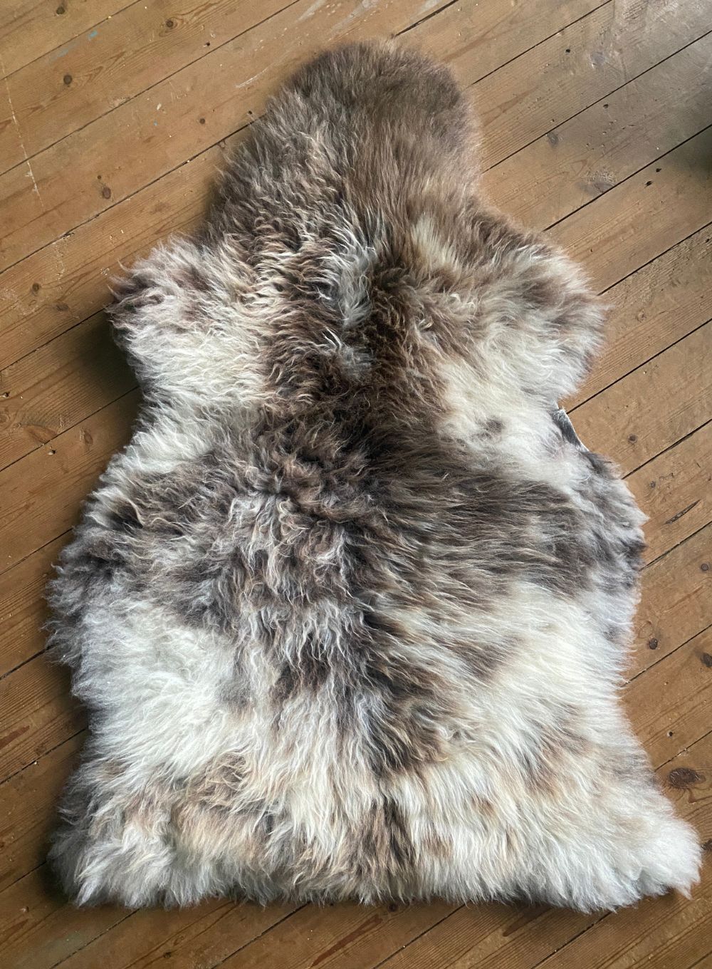 Cream and brown speckled sheepskin rug laid flat on wooden floor 