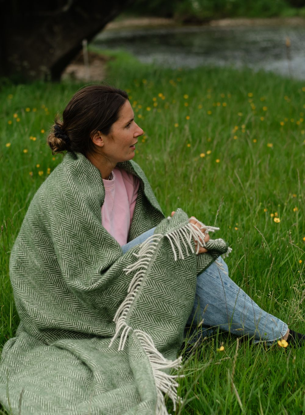 A woman wrapped in a wool blanket sitting on grass 