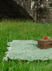 A wool blanket laid on grass with a picnic basket om top