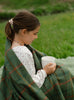 Girl wrapped in green wool blanket holding mug 