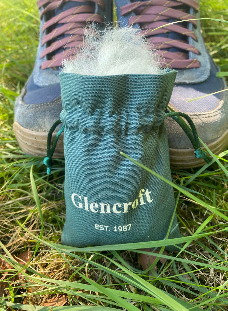 Green drawstring bag of wool on grass in front of hiking boots
