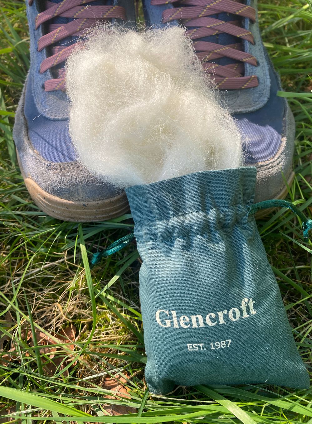 Green drawstring bag of wool on grass in front of hiking boots