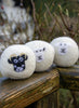 Three felted laundry balls with sheep faces on a wooden fence